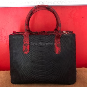 Könnte beinhalten: Eine schwarze Handtasche mit roten Griffen und Verzierungen. Die Tasche hat ein strukturiertes, schlangenartiges Muster. Die Griffe und Verzierungen sind leuchtend rot mit einem kontrastierenden Muster. Die Tasche ist rechteckig mit Reißverschluss. Der Text "RoyalHouseAtelier" ist sichtbar.