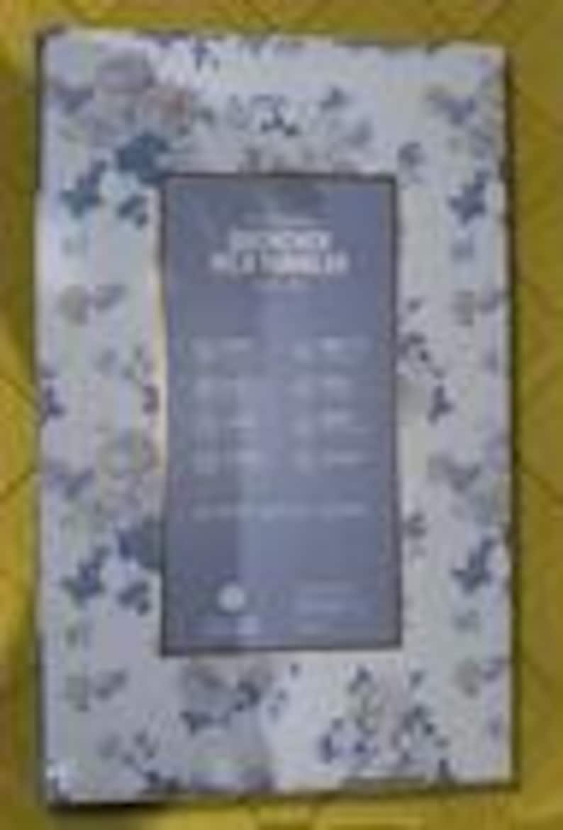 K&ouml;nnte beinhalten: Rechteckiger Bilderrahmen mit einem Blumenmuster in Blau- und Wei&szlig;t&ouml;nen. Der Rahmen hat eine zentrale &Ouml;ffnung f&uuml;r ein Foto und enth&auml;lt teilweise sichtbaren Text. Der Rahmen befindet sich auf einer gelben Oberfl&auml;che.