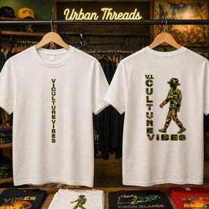 May include: White t-shirts with the text "V! CULTURE VIBES" in green and yellow. One shirt has the text vertically, the other has a graphic of a person walking with a camouflage pattern. The shirts are hanging on wooden hangers.