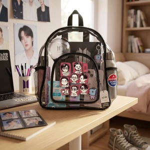 Könnte beinhalten: Ein durchsichtiger Kunststoffrucksack mit schwarzem Rand, einem Tragegriff und seitlichen Netztaschen. Die Vordertasche zeigt sechs Cartoon-Aufkleber, während das Hauptfach eine kugelförmige Leuchte, einen Schlüsselanhänger und einen runden Aufkleber enthält.