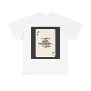 May include: White t-shirt with a playing card design. The card is a ten of spades with the text "IF YOU'RE GOING THROUGH HELL, KEEP GOING." The design is in black on a cream-coloured card.