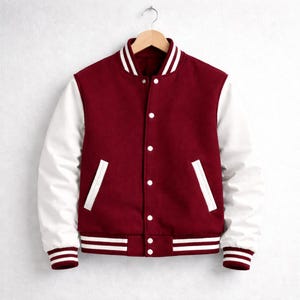Peut inclure: Veste universitaire bicolore, rouge bordeaux et blanche, suspendue à un cintre en bois. Le corps est rouge bordeaux, les manches blanches, le col et les bordures rayées blanches. Fermeture à boutons-pression blancs.