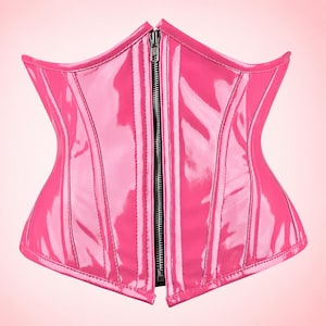 May include: A bright pink corset made of a glossy, patent-like material. The garment features vertical stitched paneling for structure and a central silver-toned metal zipper closure that runs from the top to the bottom edge.
