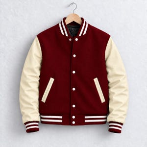 May include: A varsity jacket featuring a deep burgundy wool-blend body and contrasting cream-colored sleeves. The garment includes a snap-button front closure, two side pockets, and ribbed knit cuffs and hem with white stripes.