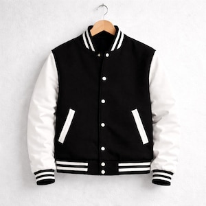 May include: A black and white varsity jacket with a button-up front, white sleeves, and white detailing on the collar, pockets, and hem. The jacket is suspended on a wooden hanger against a white backdrop.