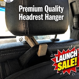 May include: A beige plastic headrest hanger attached to a black vehicle headrest, holding a black bag strap. Text reads: Made in USA, Premium Quality Headrest Hanger, Launch Sale!, Universal - Fits Most Vehicles. The hanger features a small logo.