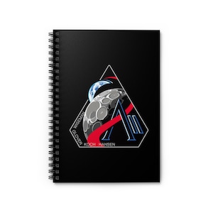 May include: Black spiral-bound notebook featuring a triangular design with a moon, Earth, and red and blue accents. The names "WISEMAN", "GLOVER", "KOCH", and "HANSEN" are printed on the notebook.