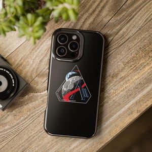May include: Black phone case with a graphic featuring a stylized moon, Earth, and the names Wiseman, Glover, Koch, and Hansen. The design includes red and blue accents within a triangular shape. The case has a glossy finish.