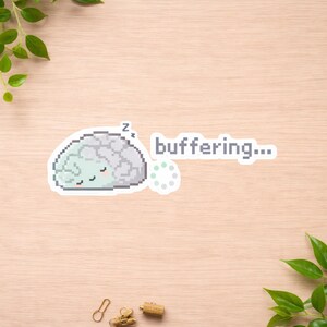 May include: A sticker featuring a pixelated brain with a sleeping expression and the word "buffering...". The brain is light green and gray, with a small "Z" above it. A loading symbol is next to the text.