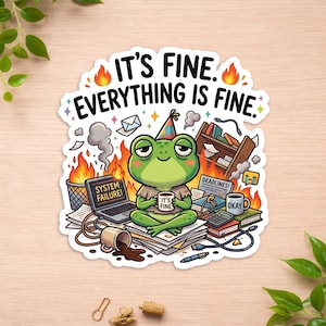 May include: A die-cut sticker featuring a green frog wearing a party hat, sitting on a stack of papers amidst a chaotic office scene with flames, a laptop displaying SYSTEM FAILURE, and mugs labeled IT'S FINE and OKAY. Text reads IT'S FINE. EVERYTHING IS FINE.