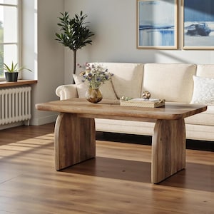 May include: A rectangular wooden coffee table with a smooth, light brown finish and a thick tabletop. The table features two solid, curved panel legs on each side, providing a sturdy base. The wood grain is visible across the surface.