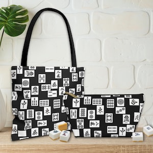 Könnte beinhalten: Eine schwarze Tragetasche und eine passende Reißverschlusstasche, beide mit einem durchgehenden Muster aus weißen Mahjong-Steinen mit schwarzen Symbolen und Schriftzeichen. Das Set ist mit mehreren losen Mahjong-Steinen davor abgebildet.
