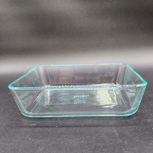 Puede incluir: Una fuente rectangular de vidrio transparente con esquinas redondeadas. El fondo de la fuente presenta el texto en relieve Pyrex, 7210, 1.5 QT, 1.4 L, NO BROILER, NO STOVETOP, MADE IN USA, 17.