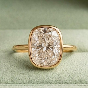 May include: A gold ring with a large, rectangular, clear gemstone. The gemstone is set in a gold bezel and has a faceted surface. The ring is displayed in a green ring box.