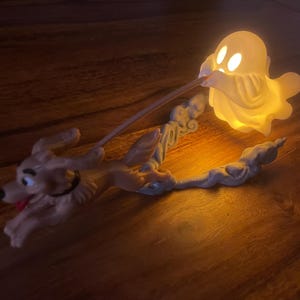 Könnte beinhalten: Eine leuchtende Figur, die einen kleinen, hellen weißen Geist zeigt, der eine Leine hält, die an einem beigefarbenen Hund befestigt ist. Der Geist strahlt ein warmes gelbes Licht aus seinem hohlen Körper aus, während der Hund rennend dargestellt ist.