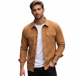 May include: A tan suede shirt with two chest pockets and button closures. The shirt is worn over a white t-shirt and paired with black pants. The sleeves are rolled up, and a silver watch is visible.