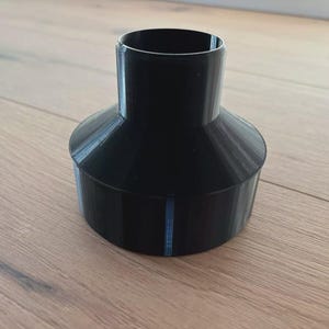 Könnte beinhalten: Ein schwarzes, trichterförmiges Objekt aus Kunststoff mit breiter Basis und schmaler Oberseite. Das Objekt hat einen zylindrischen Hals und einen ausgestellten, konischen Körper. Die Oberfläche erscheint glatt mit feinen vertikalen Linien. Das Objekt ist wahrscheinlich 3D-gedruckt.