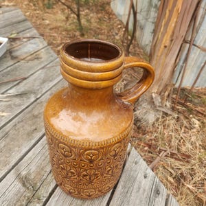 Peut inclure: Une cruche en céramique marron avec une anse. La cruche présente un motif floral texturé sur la moitié inférieure et une finition lisse et brillante. Le bord et l'intérieur sont d'un brun plus foncé.