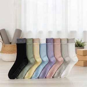 Può includere: Otto paia di calzini colorati con grip antiscivolo. I calzini sono in vari colori pastello, tra cui nero, verde, giallo, blu, viola, rosa e bianco, ognuno con un polsino grigio a contrasto. Sono disposti su una superficie di legno chiaro.