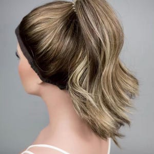 May include: A hair extension piece styled as a high ponytail with a black headband base. The hair features a blend of light brown and blonde highlights, creating a multi-tonal appearance. The ponytail is secured at the top with a clear elastic band.