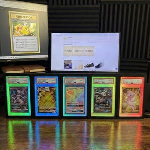 May include: A display of five Pok&eacute;mon trading cards in illuminated cases. Each card is lit with a different colour. A computer monitor shows a Pikachu card and a website. The cards are in a row.