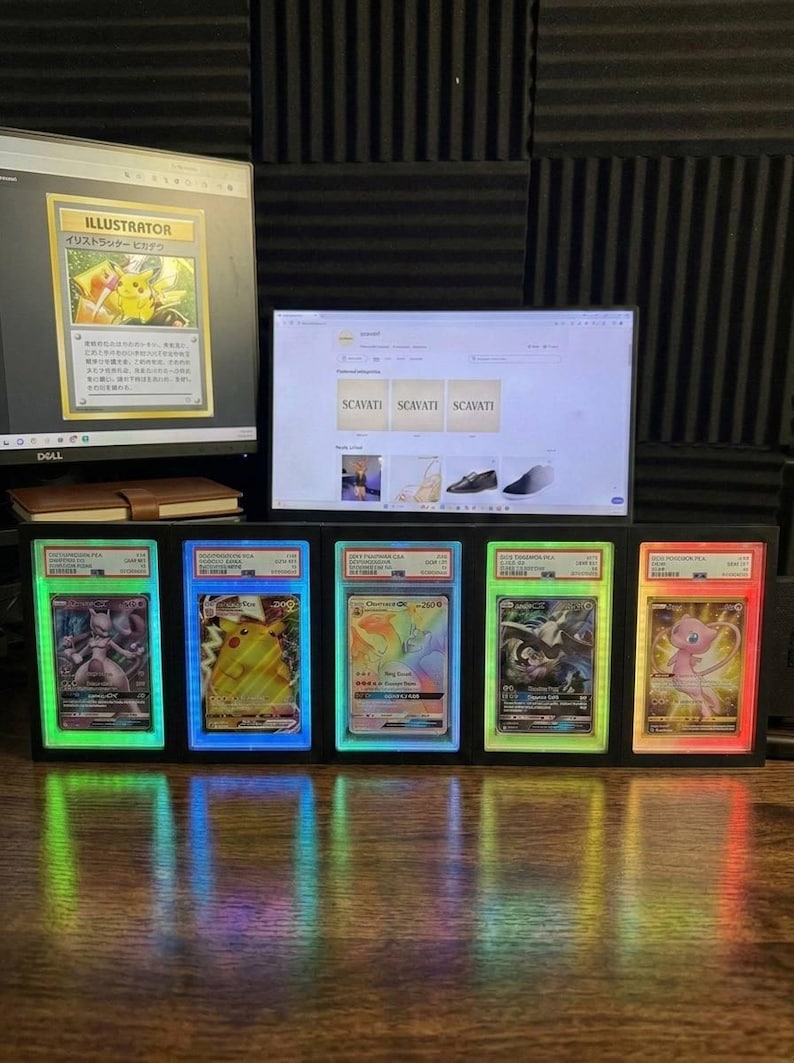 May include: A display of five Pok&eacute;mon trading cards in illuminated cases. Each card is lit with a different colour. A computer monitor shows a Pikachu card and a website. The cards are in a row.