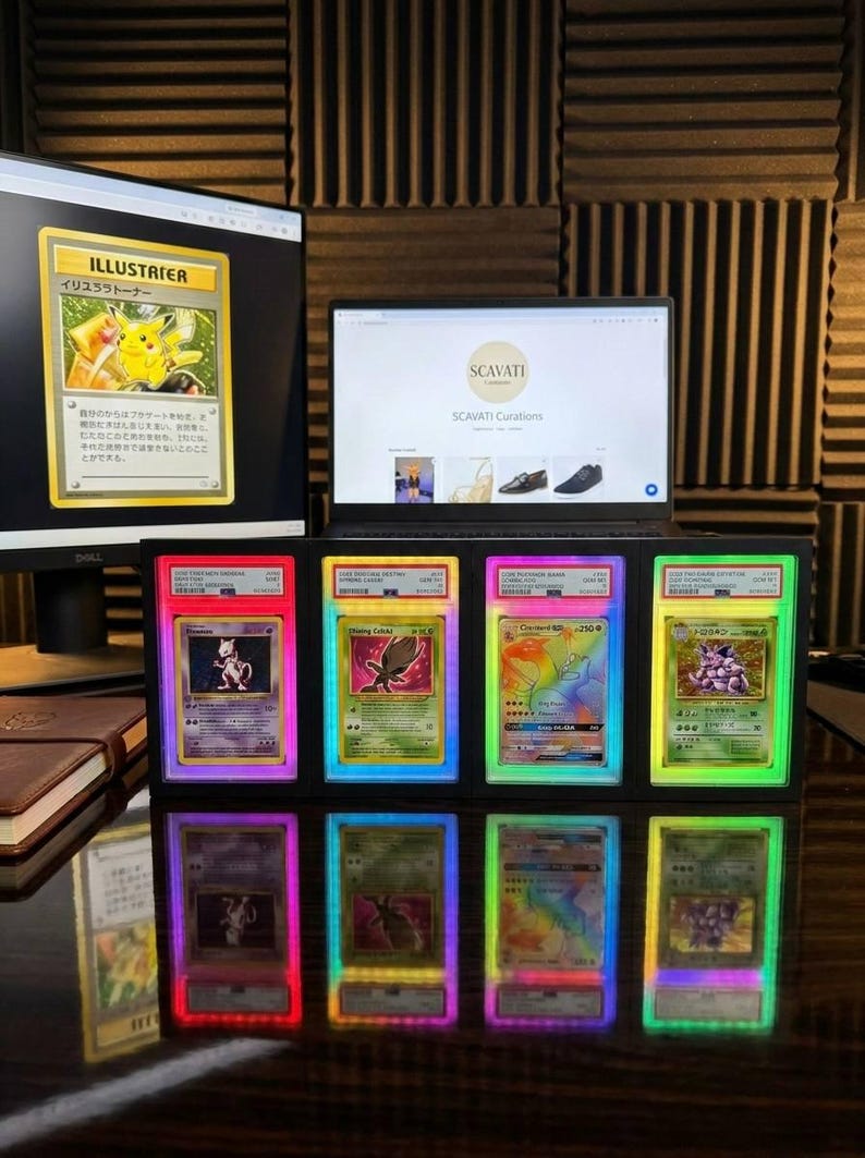 May include: A collection of graded Pok&eacute;mon trading cards, showcased with vibrant LED lighting. The display features various cards, including a Pikachu Illustrator card on a computer screen. A laptop displays the Scavati Curations website.