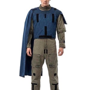 May include: A full-length shot of a person wearing a costume. The outfit includes a blue vest with black accents, a long blue cape, a long-sleeved olive green shirt, and olive green pants with black accents.