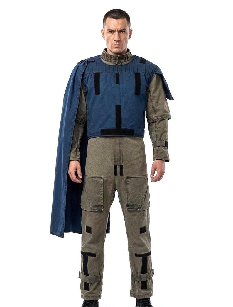 May include: A full-length shot of a person wearing a costume. The outfit includes a blue vest with black accents, a long blue cape, a long-sleeved olive green shirt, and olive green pants with black accents.