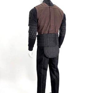 A premium galactic bounty hunter cosplay costume worn by a male model looking sideways, showcasing the screen-accurate ribbed double-sleeve detailing, dark brown flak vest, and black tailored undersuit over a solid white background.