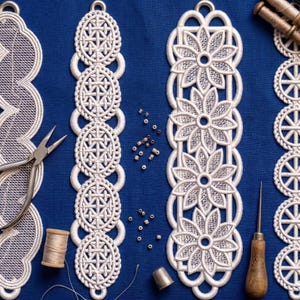 Peut inclure: Gros plan sur des marque-pages en dentelle blanche avec des motifs floraux et géométriques sur fond bleu. Les marque-pages présentent des motifs détaillés et sont reliés par des éléments circulaires. Des outils de couture, comme des ciseaux, du fil et un dé à coudre, sont également présents.