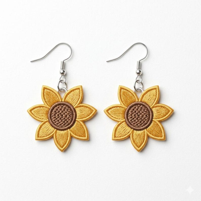 Puede incluir: Un par de pendientes de girasol. Cada pendiente presenta un girasol bordado amarillo con un centro marr&oacute;n y ganchos plateados. Los pendientes est&aacute;n sobre un fondo blanco.