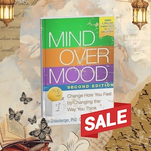 May include: A book titled Mind Over Mood Second Edition with a green, orange, and purple cover featuring a yellow smiley face emerging from a white box. The text reads Change How You Feel by Changing the Way You Think. A red banner displays the word SALE.