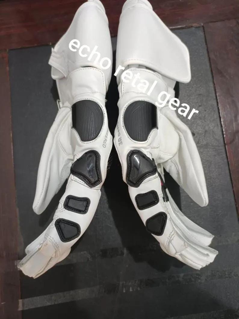 Puede incluir: Par de guantes de moto blancos con paneles protectores negros en los nudillos y las mu&ntilde;ecas. Los guantes tienen un dise&ntilde;o aerodin&aacute;mico con zonas reforzadas y el texto "echo retail gear" es visible.