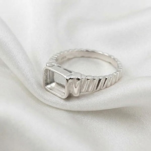 May include: A silver-toned ring featuring a rectangular setting designed for a stone or inlay. The band has a textured, ribbed pattern along the sides, and the interior of the band is clearly stamped with the hallmark 925 for sterling silver.