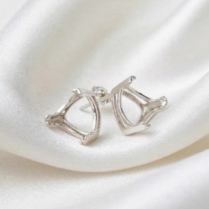 May include: A pair of silver stud earrings. Each earring has a triangular design with an open centre and a small post. The earrings are presented on white, silky fabric. The earrings are made of a silver-colored metal.