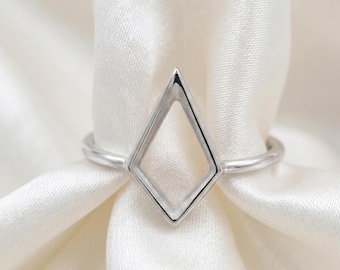 May include: A silver-toned ring featuring a geometric kite-shaped centerpiece. The ring has a smooth, polished metal band that connects to the open, diamond-like frame, creating a clean and symmetrical design with a reflective metallic finish.