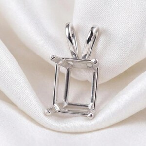 May include: A silver pendant setting with an emerald cut design. The pendant has a rectangular frame with four prongs at each corner to hold a gemstone. Two curved loops are at the top for a chain.