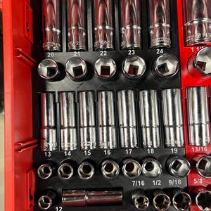 May include: A red tool organizer tray containing a collection of chrome-plated steel socket wrenches. The sockets are arranged in rows within a black plastic insert, with numerical labels printed below each slot, including sizes 12 through 24 and 7/16 to 13/16.