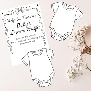 Op de afbeelding: Een babyshower-activiteitenset met een bord met de tekst "Help Us Decorate Baby's Dream Outfit". Twee blanco babyrompers zijn inbegrepen. Gasten worden uitgenodigd om de rompers te versieren en berichten te schrijven.