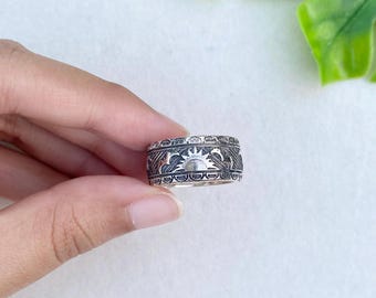 Könnte beinhalten: Ein silberfarbener Metallring mit einem geprägten Design aus Sonne und Mondsichel, umgeben von komplizierten geometrischen Mustern. Das Band hat ein breites, flaches Profil mit einem dunklen, oxidierten Finish in den vertieften Bereichen.