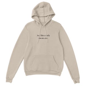 May include: A beige hooded sweatshirt with a drawstring hood and a front pocket. The text "Act like a lady, think like a Boss" is printed in black on the front. The sweatshirt is made of a soft fabric.
