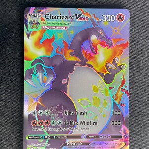 Peut inclure: Une carte à collectionner holographique Charizard VMAX représentant un Charizard sombre avec des flammes orange, 330 PV, et des attaques incluant Claw Slash et G-Max Wildfire. La carte affiche le texte SV107/SV122 et 2021 Pokemon/Nintendo/Creatures/GAME FREAK.