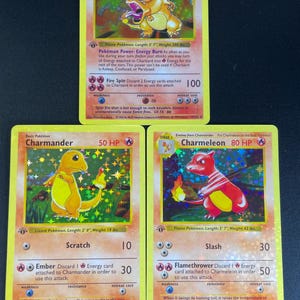 May include: Three holographic Pokémon trading cards featuring Charizard with 120 HP, Charmander with 50 HP, and Charmeleon with 80 HP. Each card displays the character illustration, name, HP value, attack moves, and descriptive text in English.