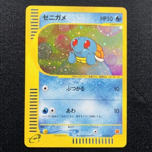 May include: A Japanese Squirtle Pokemon trading card with a yellow border and a holographic illustration of the blue turtle character. The card displays the name Zenigame, HP50, and two water-type attacks with Japanese text and numerical values.