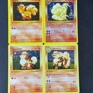 Puede incluir: Cuatro cartas coleccionables Pokémon holográficas con Vulpix, Ninetales, Growlithe y Arcanine. Cada carta muestra la ilustración del personaje, valores de HP, nombres de ataques, números de daño y texto descriptivo en inglés sobre un fondo amarillo.