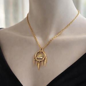 Pode incluir: Colar com pingente dourado com um design circular, um triângulo e pontas penduradas. O colar é exibido em um manequim, destacando os detalhes intrincados e os elos delicados da corrente. O pingente tem uma estética vintage.