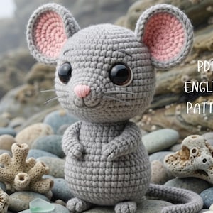 May include: A crocheted gray mouse with pink inner ears, a pink nose, and large black eyes. The mouse has a long tail and is sitting on a bed of rocks. The text "PDF ENGLISH PATTERN" is visible.