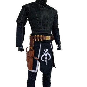 May include: Black costume with a high collar, long sleeves, and a decorative stitched design. The costume includes a brown belt with gold accents and a holster. A black and white graphic is on the front of the costume.