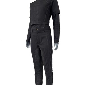 May include: A black two-piece outfit consisting of a cropped long-sleeve top and matching trousers. The top features a high collar and structured shoulders, while the pants have a fitted waistband and visible seam detailing throughout the garment.